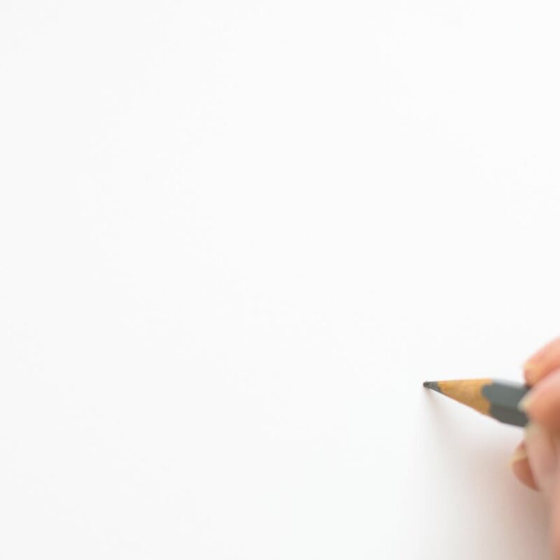 Close-up of a hand sketching on white paper with a pencil, emphasizing creativity.